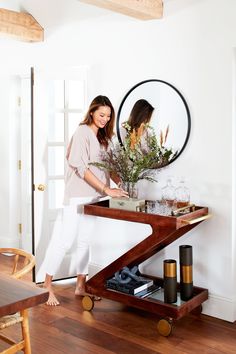 a woman standing in front of a mirror with flowers on the table next to her