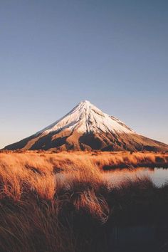 a mountain with snow on top and brown grass in the foreground, near a body of water