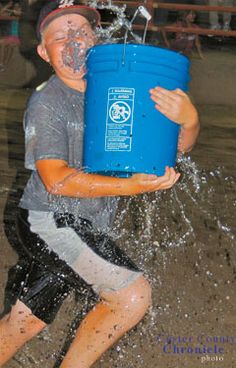 a young boy is playing in the water with a blue pail and splashing water on his face