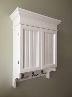 a white wall mounted cabinet with two hooks on it's front and back sides