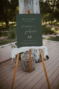 an easel with a seating chart on it sitting on a wooden deck in front of a tree