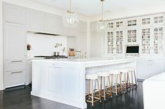 a kitchen with white cabinets and marble counter tops, bar stools in front of the island