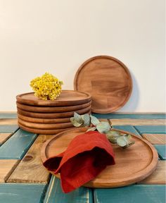 wooden plates stacked on top of each other next to a red cloth and yellow flower