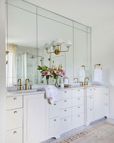 a bathroom with two sinks, mirrors and flowers in vases on the counter top