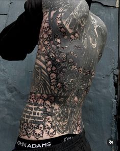 the back of a man with tattoos on his body and chest is covered in skulls