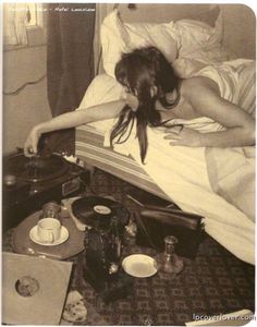 a woman laying in bed next to an old record player and other items on the floor