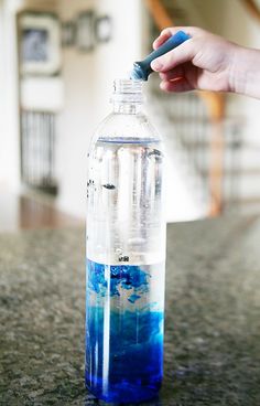 a hand is holding a blue and white substance in a water bottle on the counter