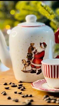 a tea pot and cup on a table with coffee beans in front of the kettle