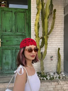 a woman wearing sunglasses and a red crochet headband standing in front of a cactus