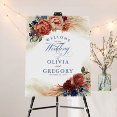 a welcome sign with flowers on it in front of a white wall and string lights