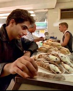 a man sitting at a table with many pastries on it and people in the background