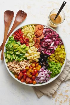 a large bowl filled with lots of different types of vegetables next to two spoons