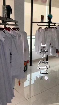 there are many white shirts hanging on the rack in this storefront window, with arabic writing above them