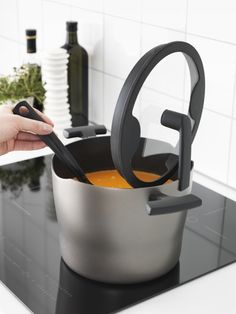 a woman is holding an orange in a large pot on the stove with a black handle