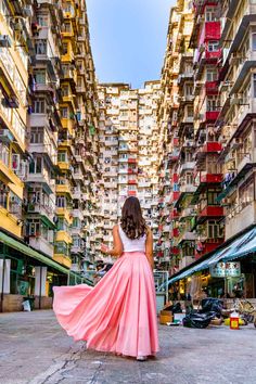 a woman in a long pink skirt is walking through an alley way with tall buildings