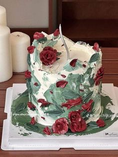 a white cake with red flowers on it sitting on top of a table next to candles