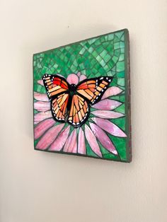 a stained glass butterfly sitting on top of a pink flower in a green and white background