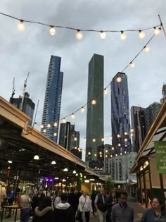 many people are walking around in the city at dusk or dawn with lights strung above them