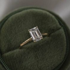 an emerald cut diamond ring sits on top of a green velvet case