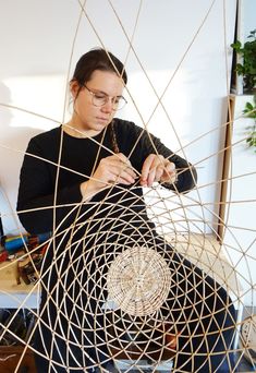 a woman sitting on the floor working on an object with wire in front of her