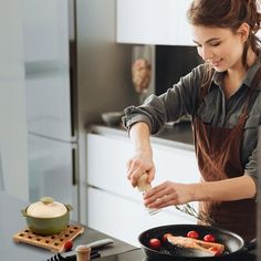 a woman in an apron is cooking food on a skillet