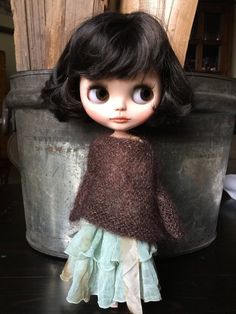 a close up of a doll on a table near a potted plant and wooden fence