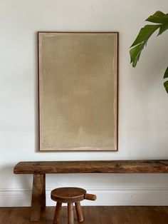 a wooden bench in front of a painting on the wall next to a potted plant