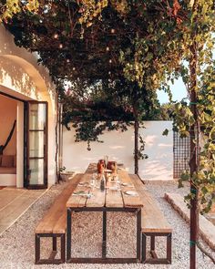 a wooden table sitting under a tree next to a white wall with lights on it