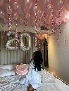 a woman sitting on top of a bed under balloons