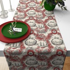 a table with a red plate on it next to a vase filled with flowers and greenery