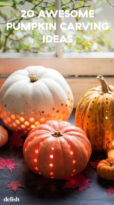 some pumpkins are lit up and sitting on the ground with leaves around them in front of a window