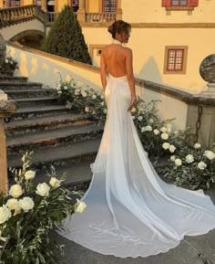 the back of a woman's wedding dress in front of some stairs and flowers