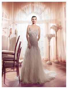 a woman standing in front of a window wearing a white dress with feathers on it