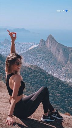 a woman sitting on top of a mountain with her arms in the air