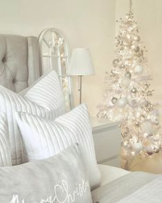 a white christmas tree in a bedroom next to a bed with pillows and blankets on it