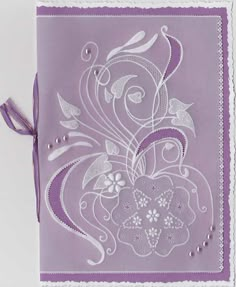 a purple and white greeting card with an intricate floral design on the front, tied in a ribbon