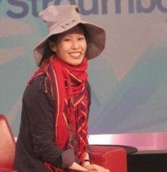 a woman wearing a hat and scarf sitting on a red chair in front of a screen