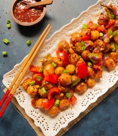 chicken and vegetable stir fry served with chopsticks on a white platter next to a bowl of sauce