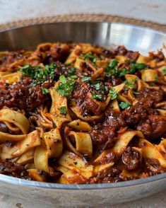 a metal bowl filled with pasta covered in sauce and meat toppings on top of a table