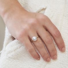 a woman's hand with a pearl ring on top of her finger, wearing a white sweater