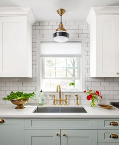 a kitchen with white cabinets and gold faucets on the windowsill, along with green plants