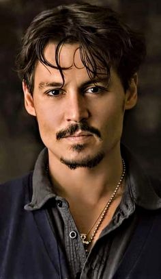 a man with a moustache on his face wearing a black shirt and necklace