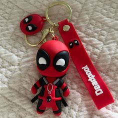 a red deadpool keychain sitting on top of a white bed next to a pair of scissors