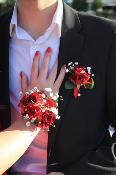 a man and woman wearing red roses on their wedding day, one holding the other's hand