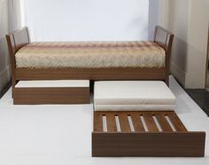 a bed sitting on top of a white floor next to a wooden footstool