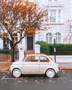 an old car is parked in front of a white house with autumn leaves on the ground