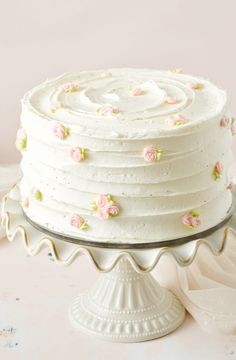 a white frosted cake with pink flowers on it sitting on a table next to a plate