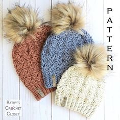 three crocheted beanies with two pom - poms are laying on a white wooden surface