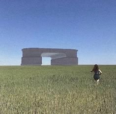 a woman is flying a kite in the middle of a field with an enormous structure behind her