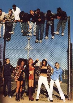 several people standing on top of a chain link fence with their arms in the air